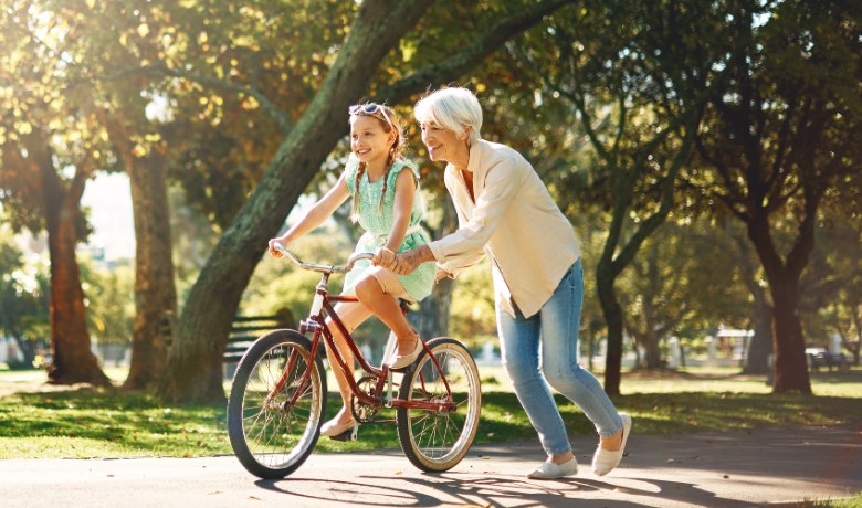 A grandmother helping a child ride a bicycle in a sunlit park