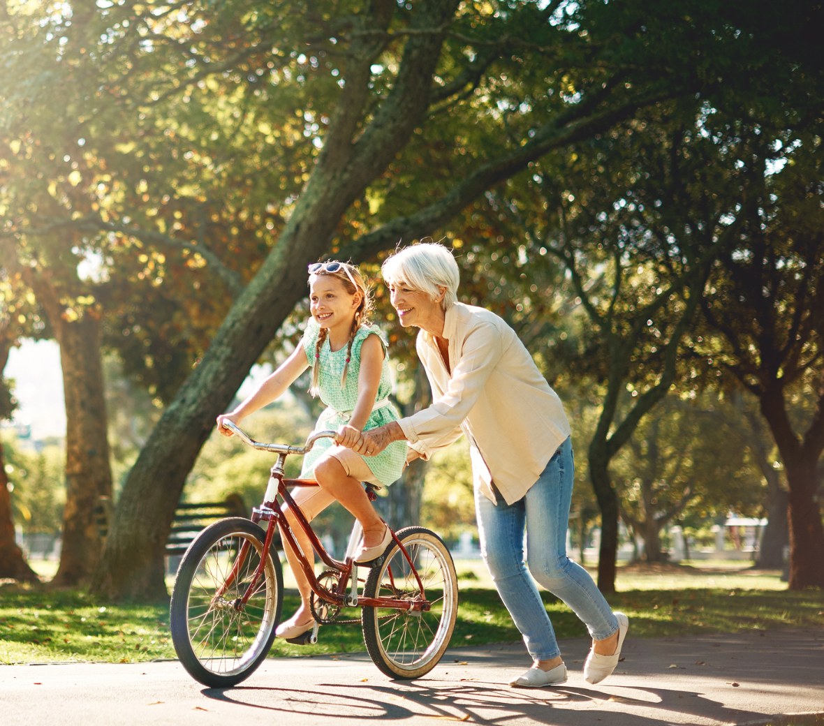 A grandmother helping a child ride a bicycle in a sunlit park